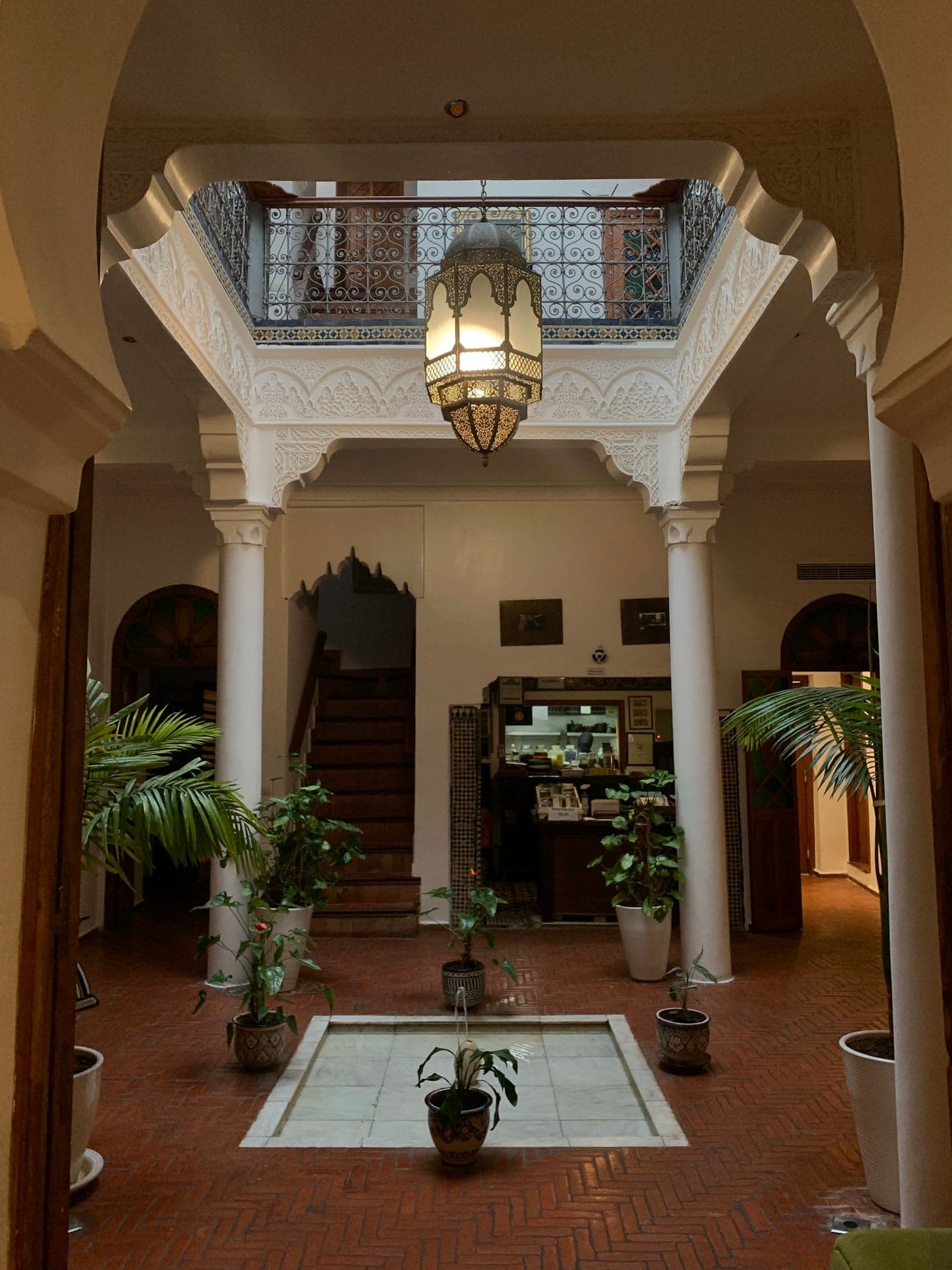 warm courtyard of a traditional Marrakech riad with a glowing filigree lantern, hand-carved plasterwork, and a terracotta tiled floor