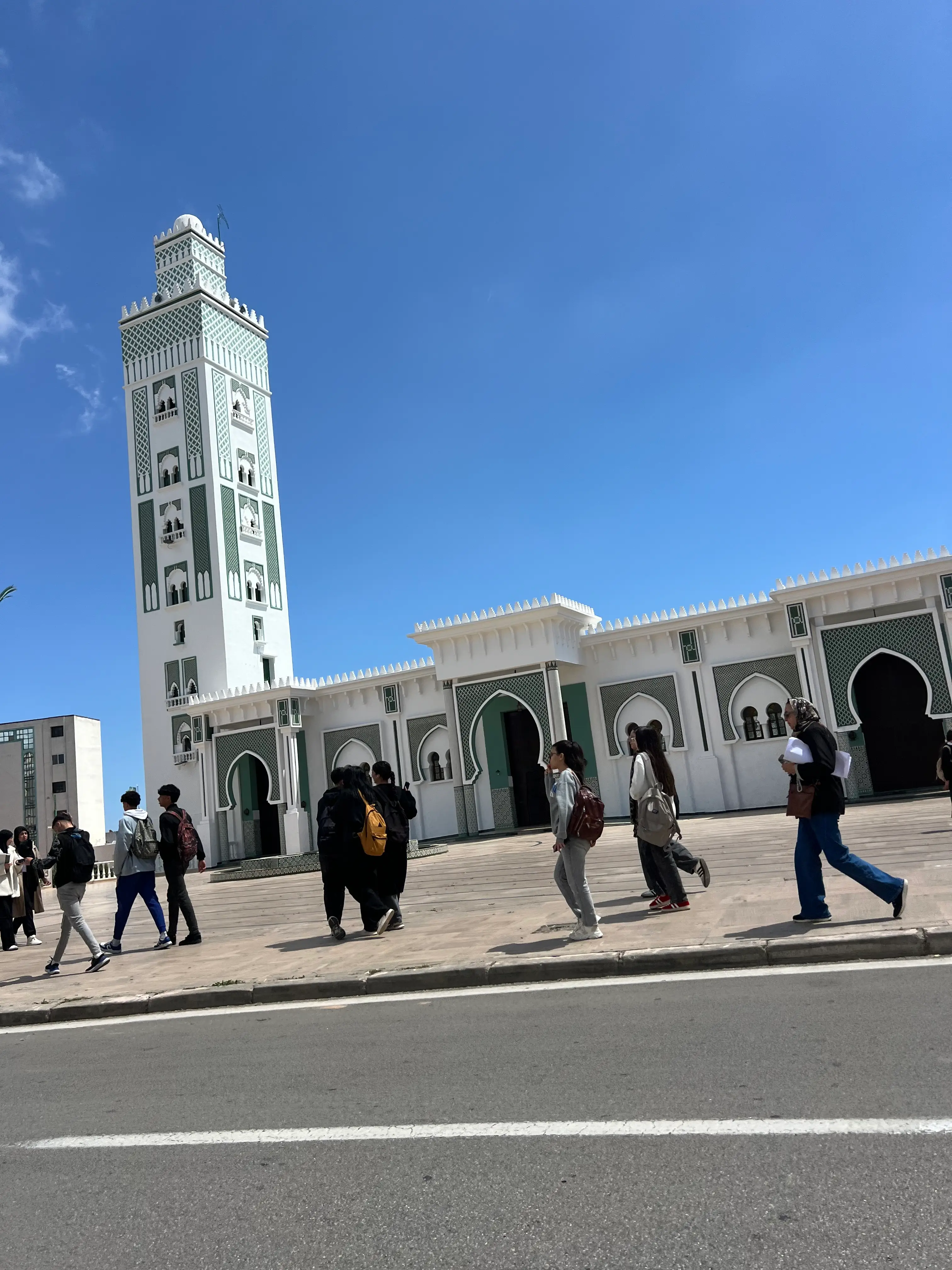 Travelers walking beside the Grand Mosque of Tangier under a clear blue sky