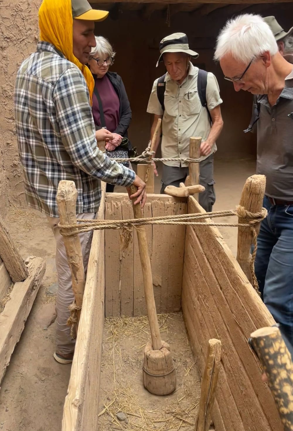 Guests listening closely as a local host demonstrates a traditional wooden tool in an earthen home