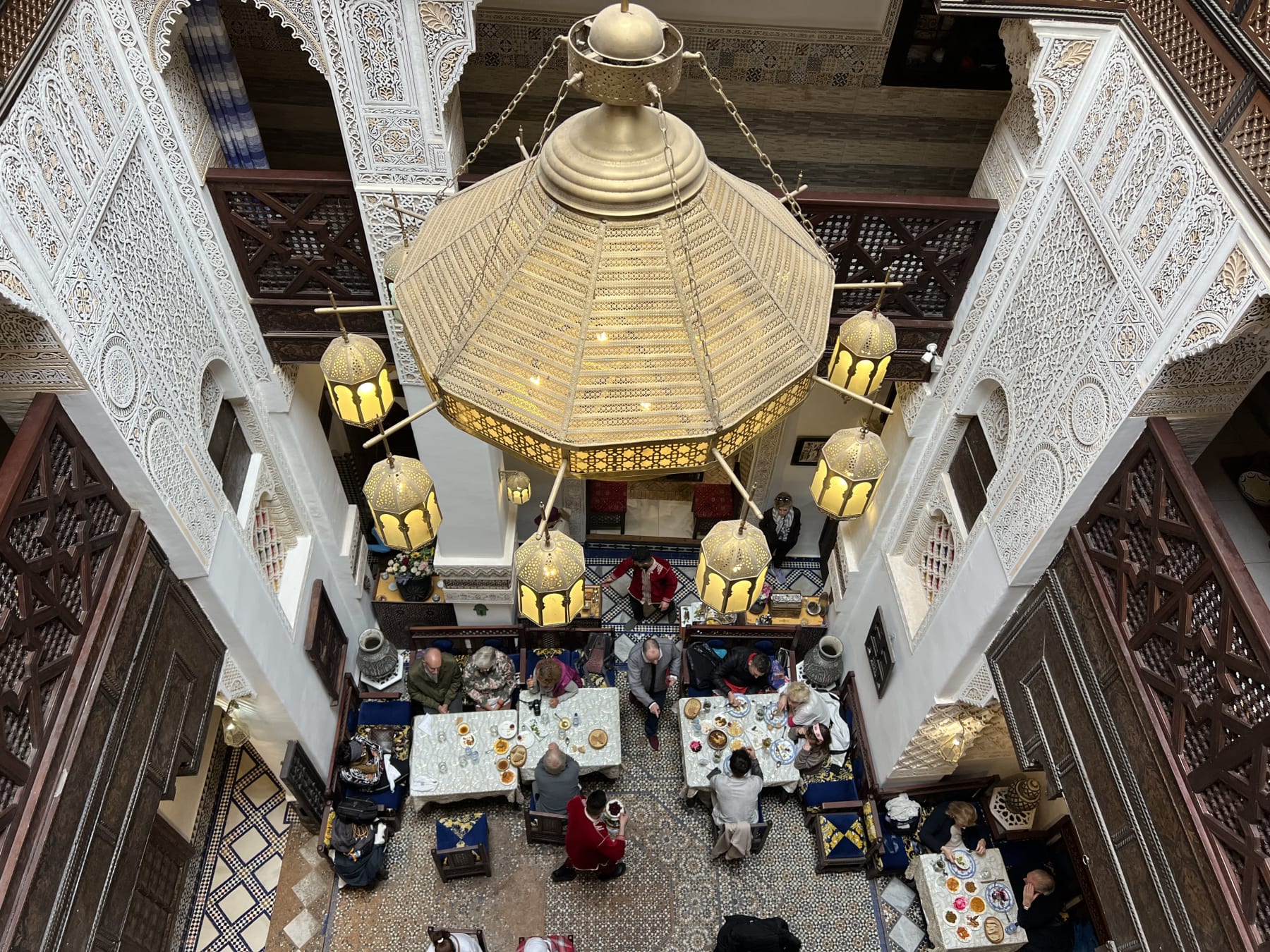 Guests dining beneath carved plasterwork and glowing lanterns in an ornate Moroccan riad courtyard